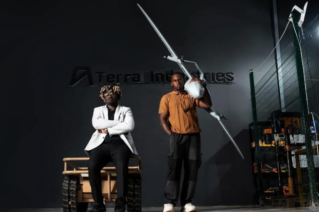 Two young men, co-founders of Terra Industries, pose inside their Abuja facility. One is seated, the other standing ad holding a small aircraft drone.